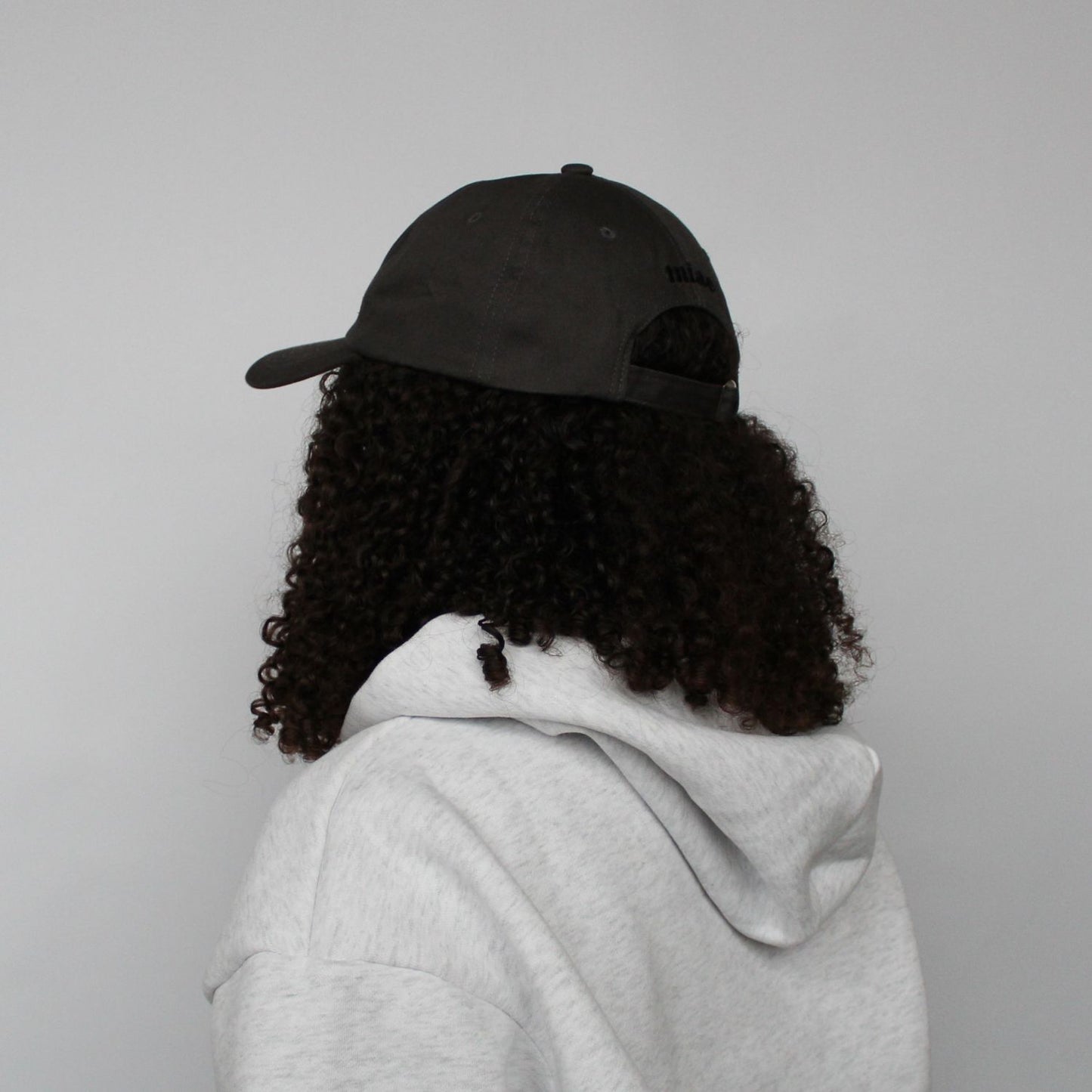Diagonal back view of the Miae Charcoal Satin-Lined Cap, showcasing the logo and adjustable fit, with a curved visor that enhances facial features.