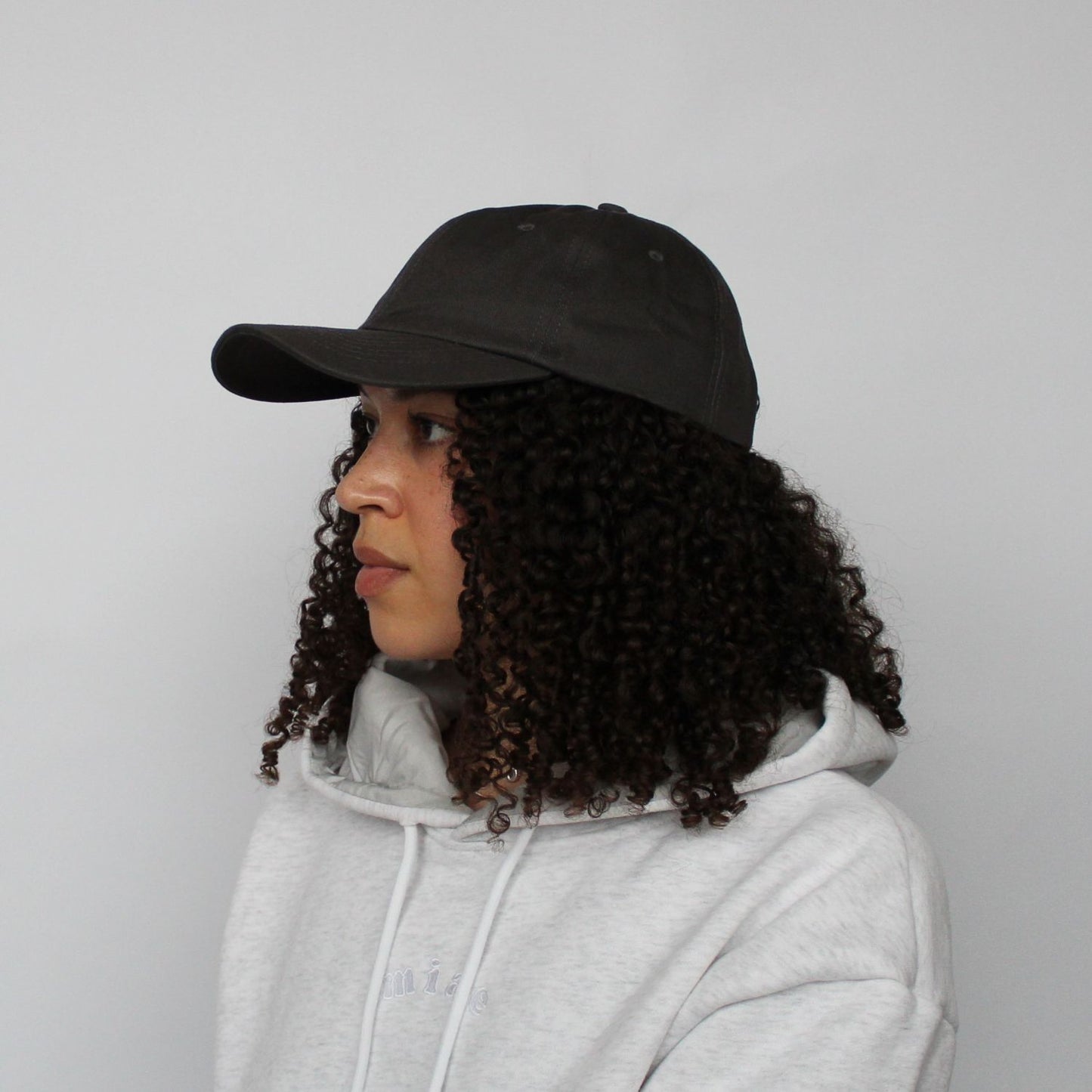 Model in the Miae Charcoal Satin-Lined Cap, designed with a curved visor for a face-flattering fit and satin lining to prevent frizz and retain moisture.