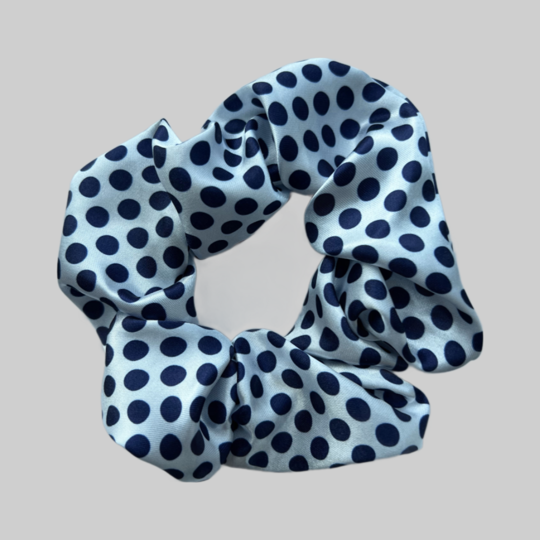 Flat lay of the Miae White Satin Scrunchie with blue polka dots, a soft and elegant hair tie designed to protect against breakage and frizz.