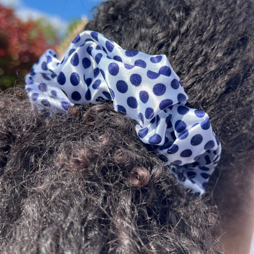 Model wearing the Miae White Satin Scrunchie with blue polka dots in a ponytail, a smooth and protective hair accessory for textured and curly hair.
