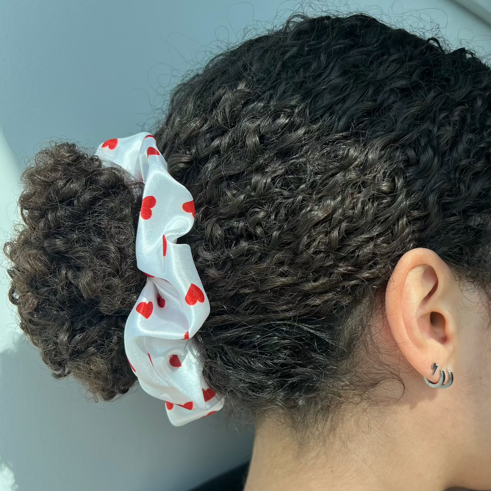 Curly ponytail secured with the Miae White Satin Scrunchie with red love hearts, offering a smooth and gentle hold while reducing breakage.