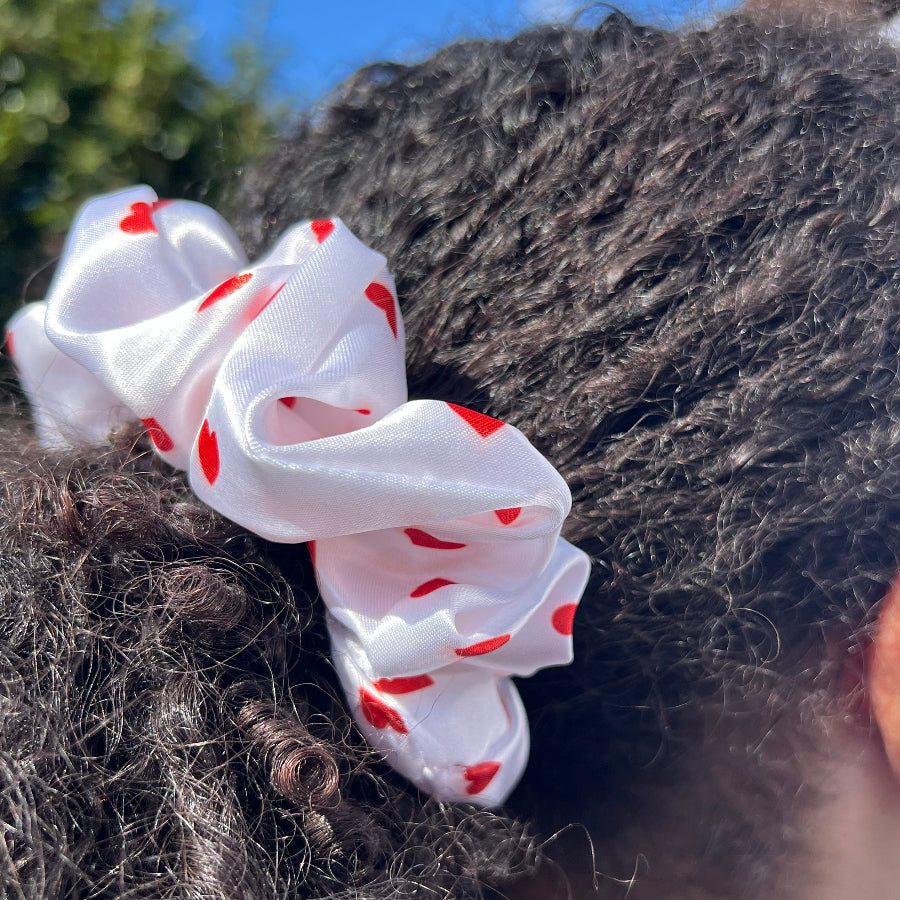 Side view of a curly ponytail styled with the Miae White Satin Scrunchie with red love hearts, designed to be both stylish and protective.