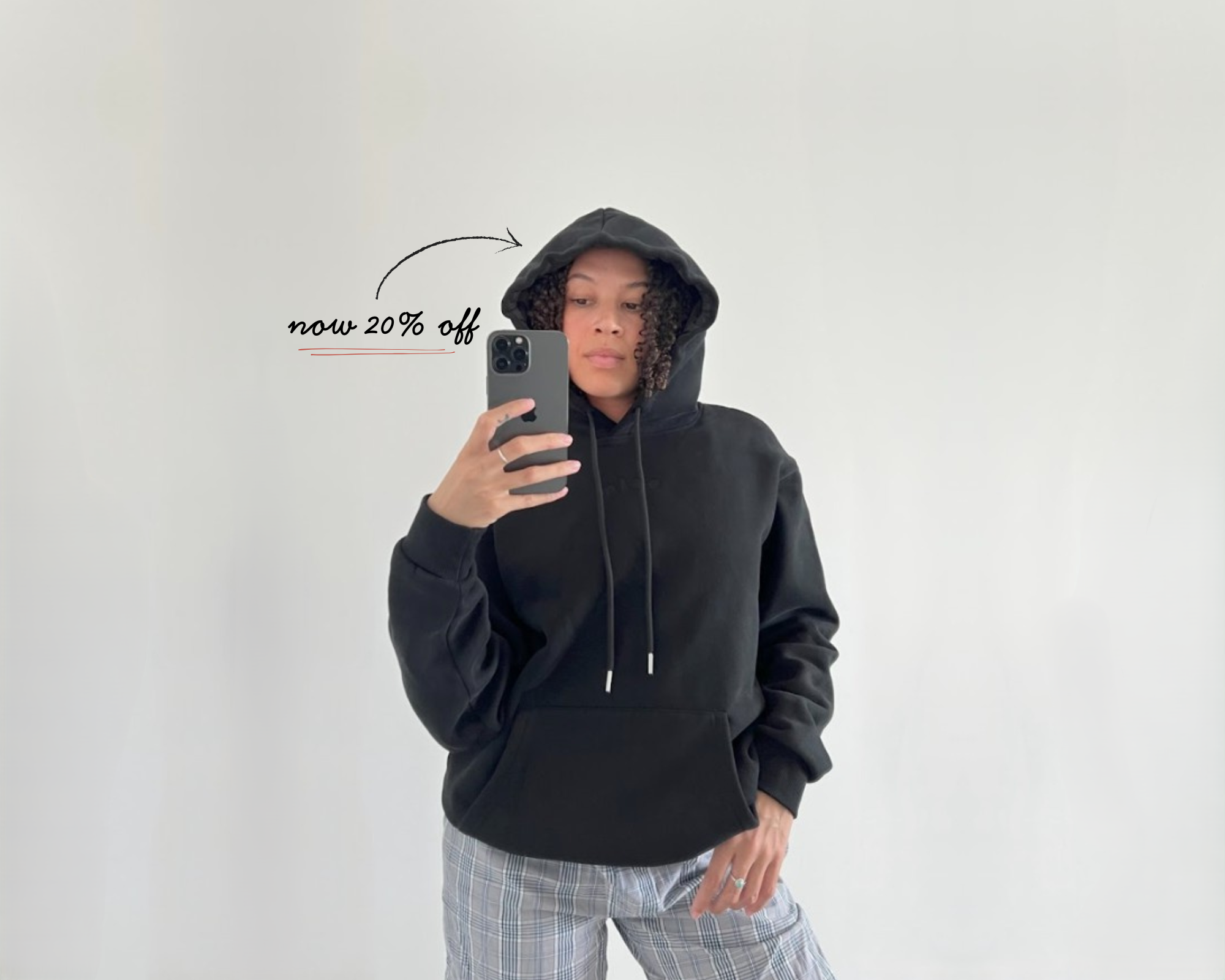 Person wearing a black satin lined hoodie taking a mirror selfie on a plain background with a discount text overlay
