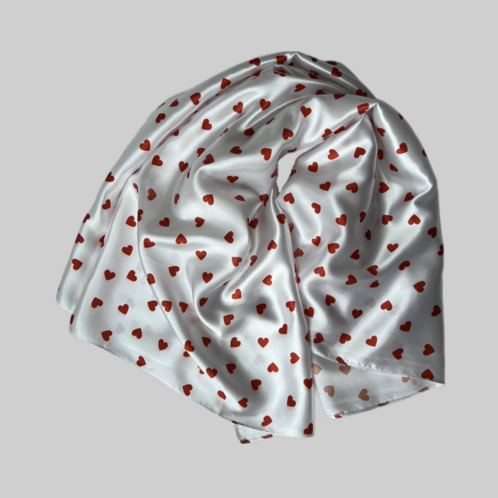 Flat lay of the Miae White Satin Hair Scarf with red love hearts, a soft and protective accessory for curly and textured hair.