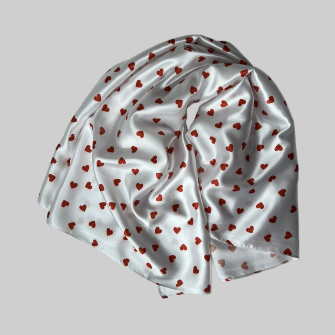Flat lay of the Miae White Satin Hair Scarf with red love hearts, a soft and protective accessory for curly and textured hair.