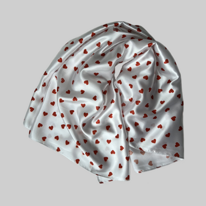 Flat lay of the Miae White Satin Hair Scarf with red love hearts, a soft and protective accessory for curly and textured hair.
