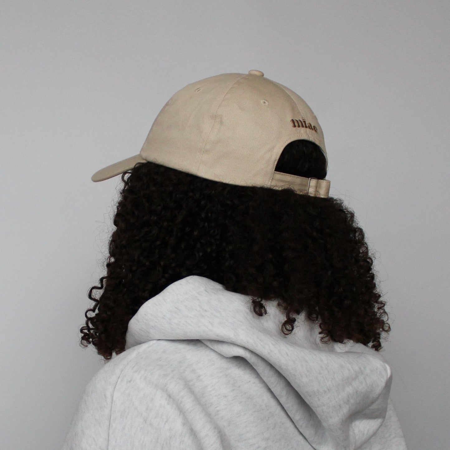 Back view of the Miae Beige Satin-Lined Cap, featuring an adjustable strap, logo detail, and a soft unstructured fit that flatters the face and protects natural, textured, and curly hair.