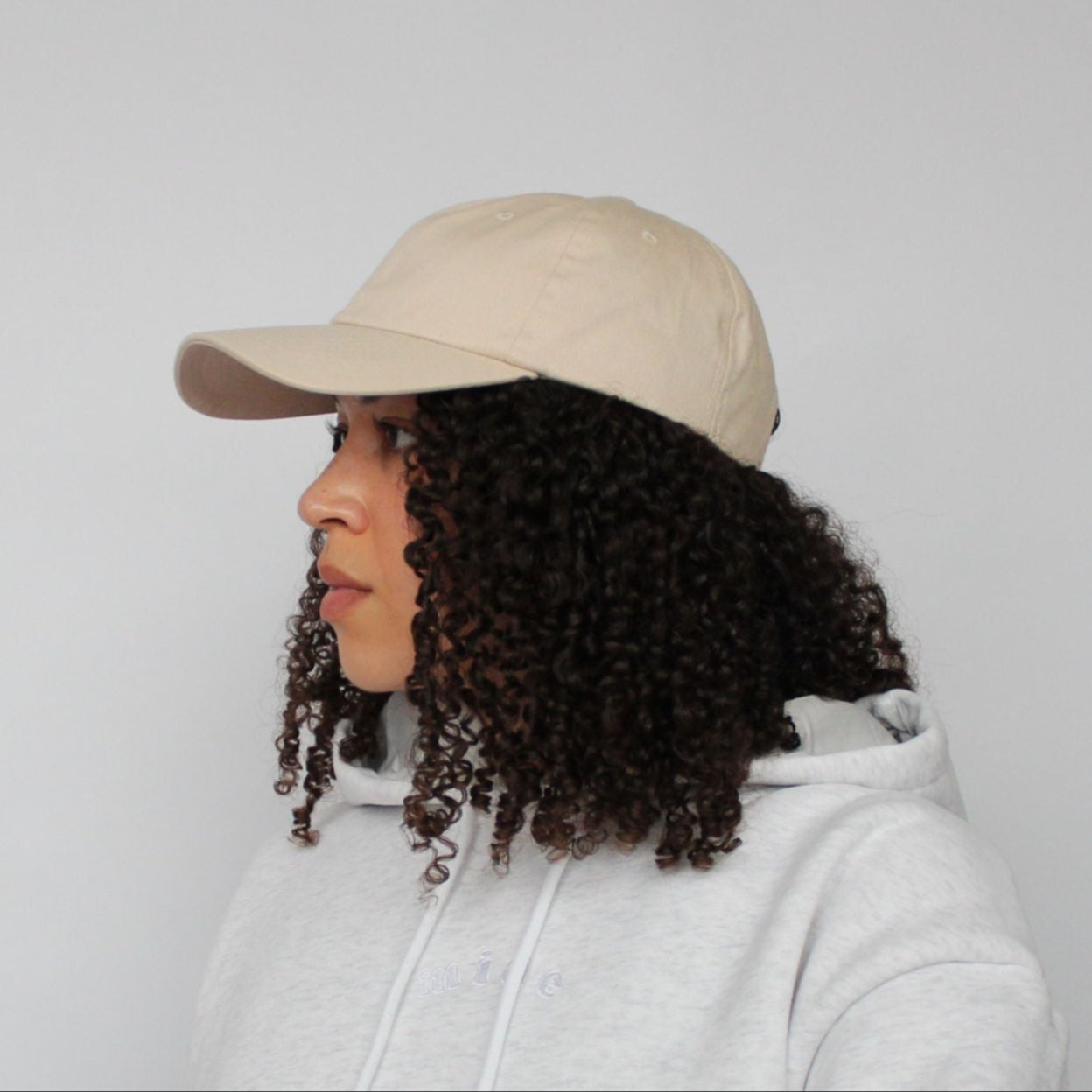 Model wearing the Miae Beige Satin-Lined Cap, an unstructured cap with a curved visor that flatters the face while protecting natural, textured, and curly hair.