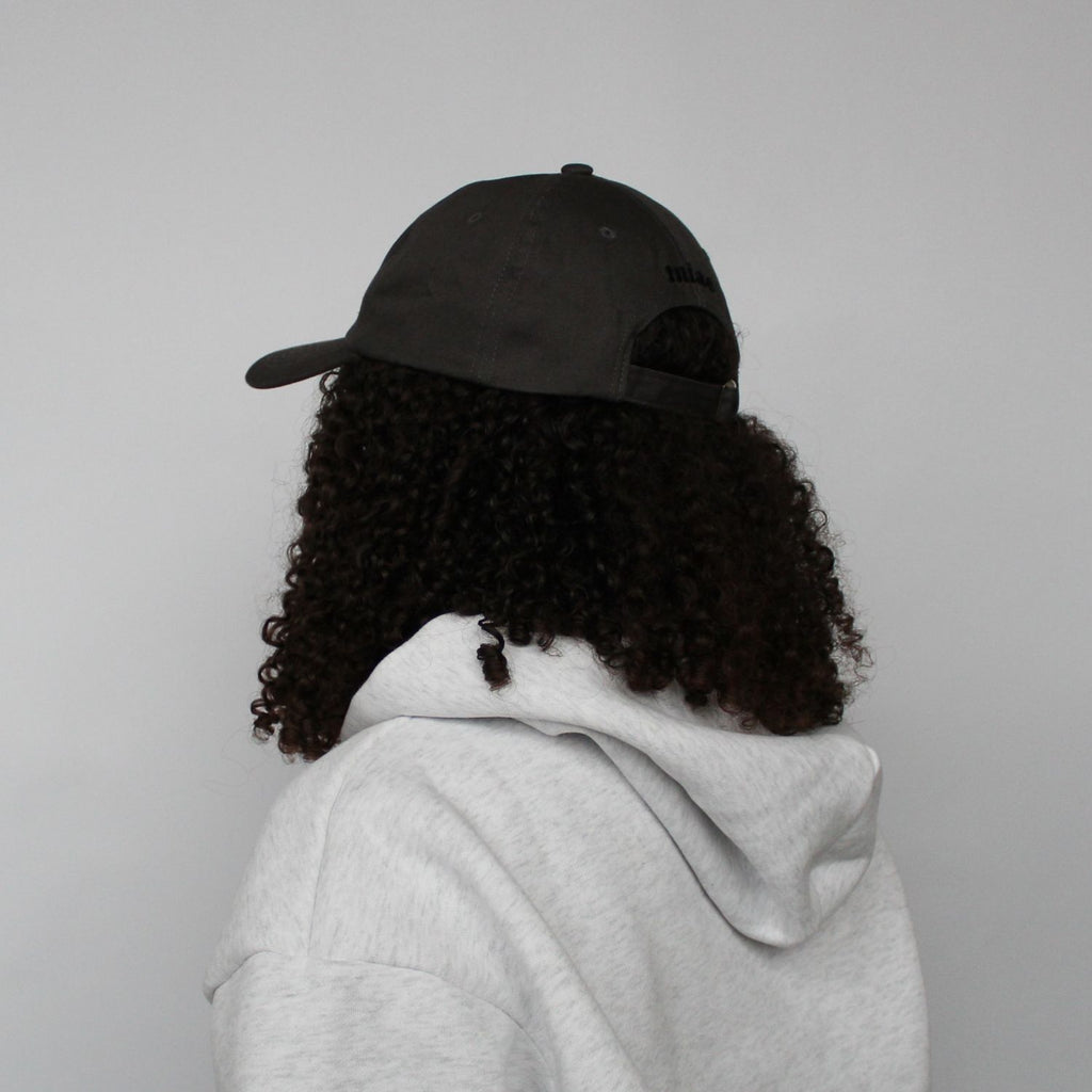 Diagonal back view of the Miae Charcoal Satin-Lined Cap, showcasing the logo and adjustable fit, with a curved visor that enhances facial features.