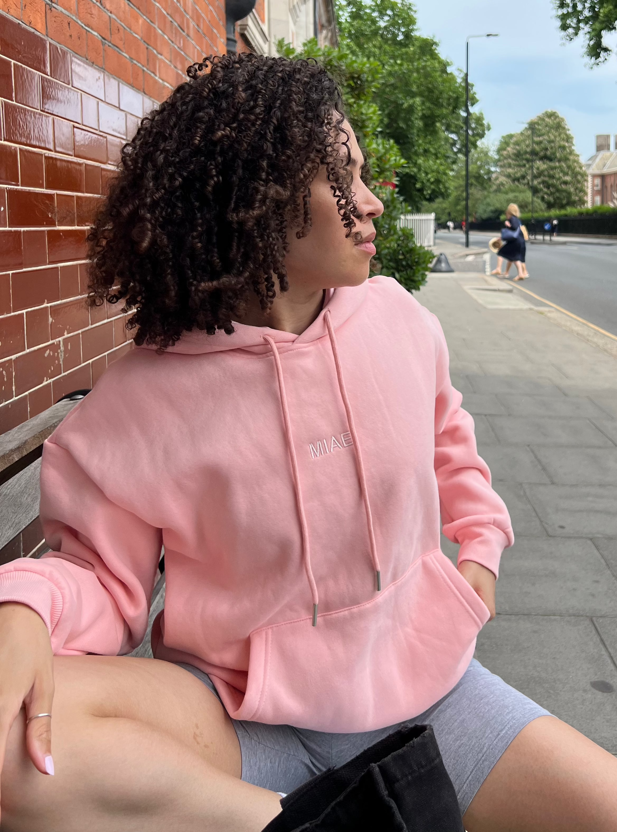 Model wearing the Miae Pink Satin-Lined Hoodie in a casual setting, designed to protect natural, textured, and curly hair by reducing frizz, dryness, and breakage