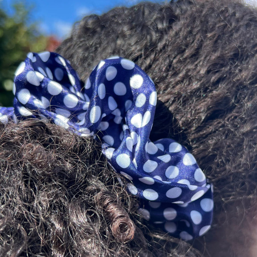 Curly hair styled in a ponytail with the Miae Blue Satin Scrunchie featuring white polka dots, offering a gentle hold while minimizing frizz