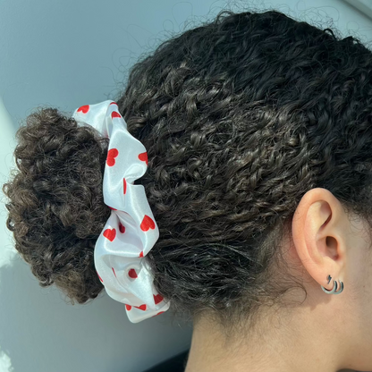 Curly ponytail secured with the Miae White Satin Scrunchie with red love hearts, offering a smooth and gentle hold while reducing breakage.